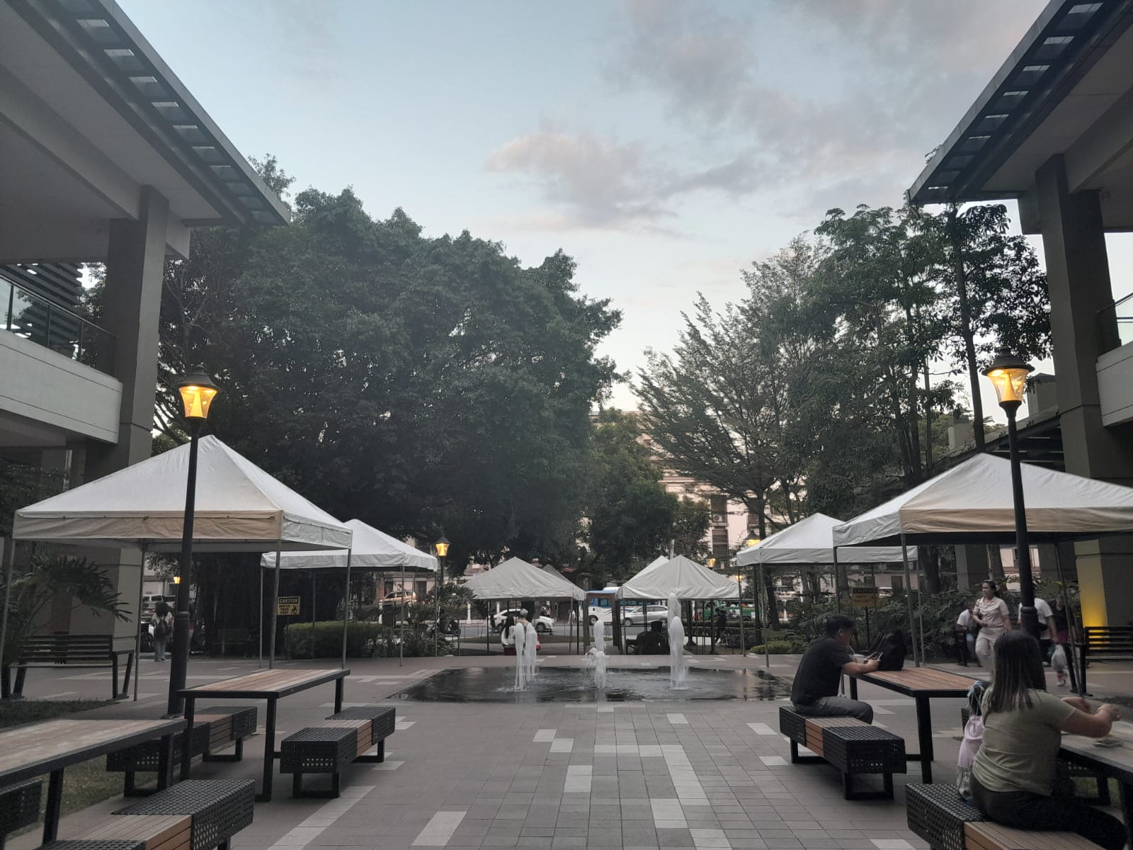 The back portion of Ayala Malls Capitol Central consists of benches with umbrellas and a fountain at the center. I believe it lights up at night. The image was taken in the early evening. Plenty of people visited and ate at the mall at the time.