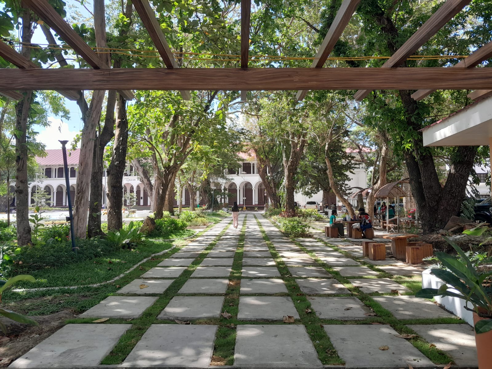 The "mini forest", now known as WVSU Alumni Park. A cobblestone path leads straight to Quezon Hall. On either side of the path lie benches for students to sit and have conversations or complete assignments. The old mini forest looked different: just bare dirt with a patch of grass and stone. There were benches but not as organized as it is now.
